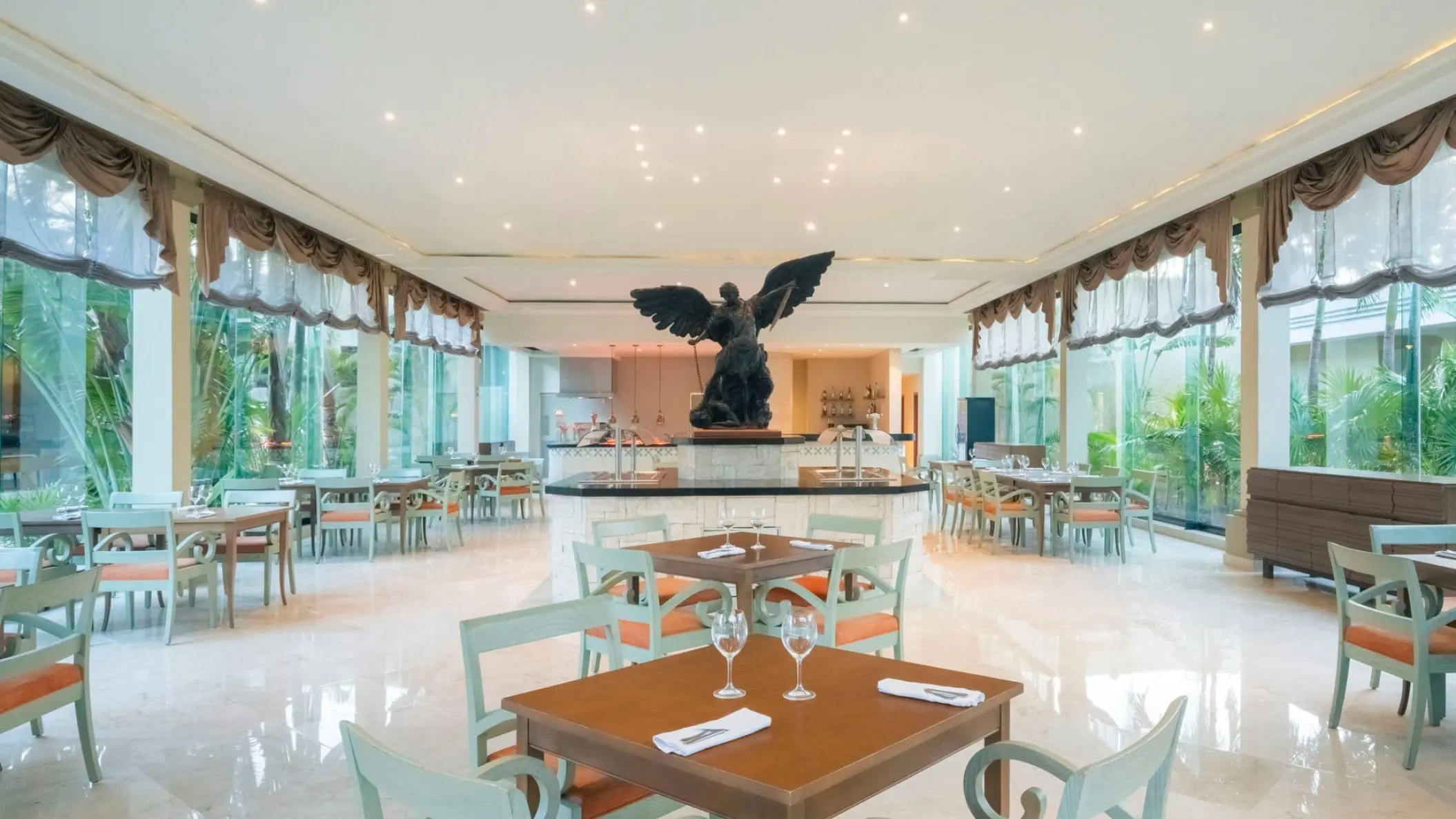 Indoor restaurant dining room with large windows and a winged statue at Iberostar Quetzal, Playa Del Carmen