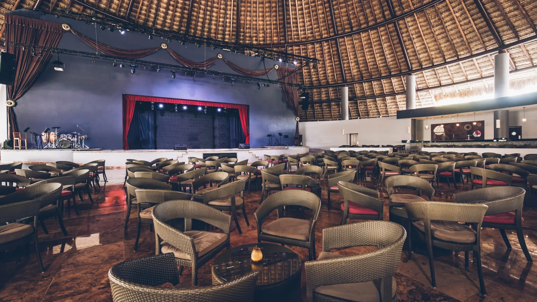 Indoor theater with a stage and wicker seating under a thatched palapa roof at Iberostar Selection Cancun