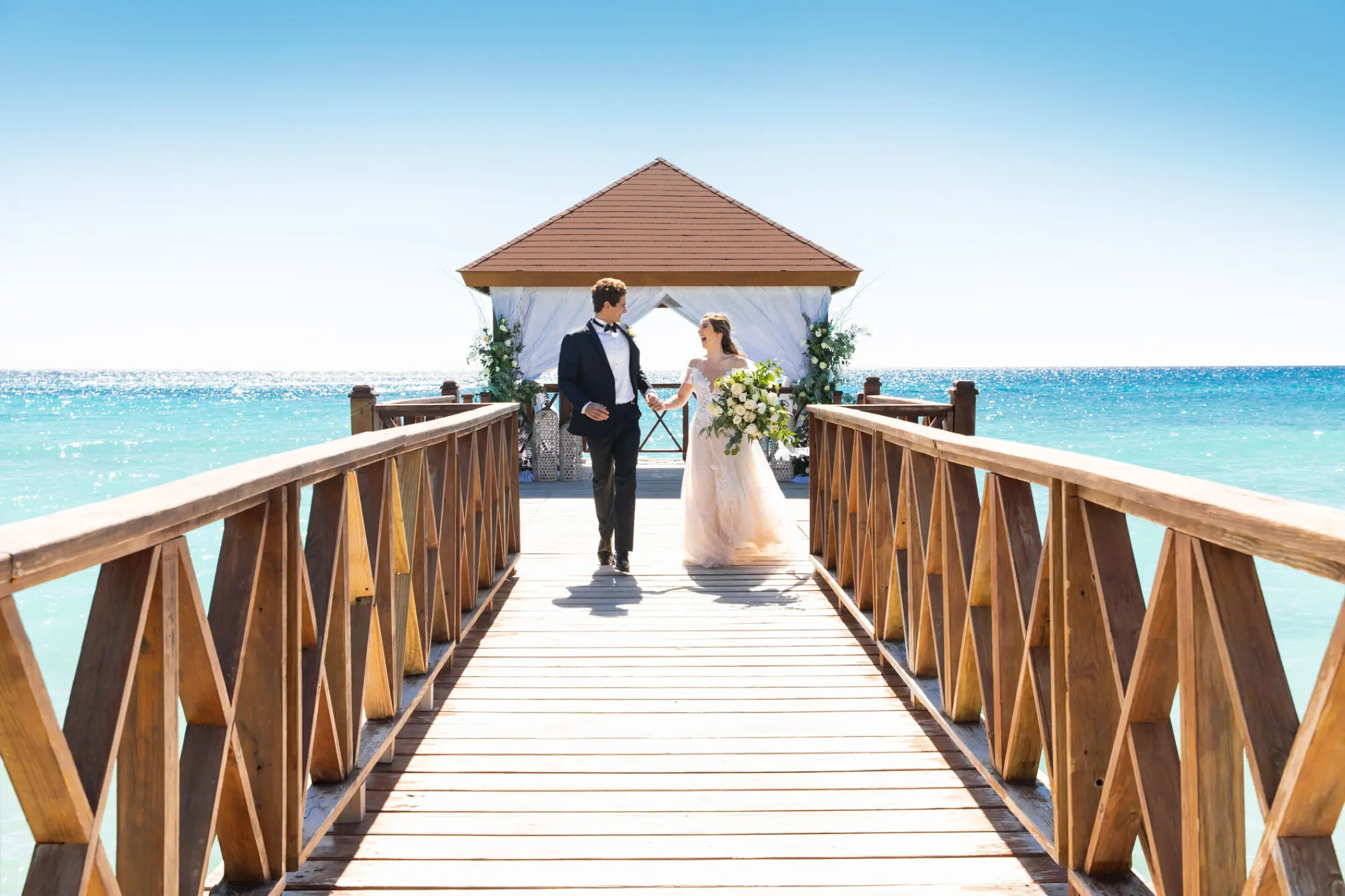 Bride and groom walking on a wooden pier gazebo at Iberostar Selection Cancun