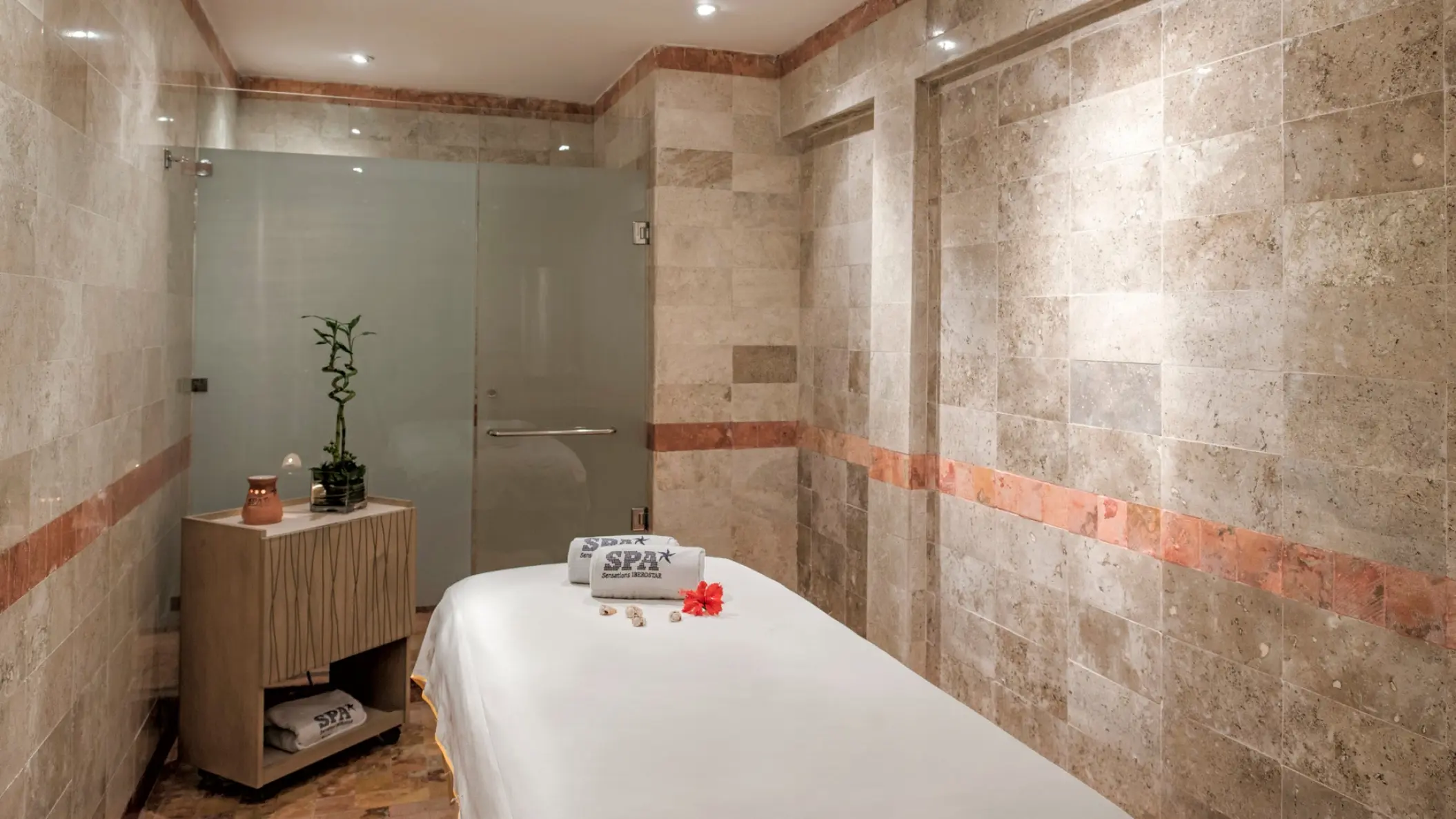Spa massage table with rolled towels and a hibiscus flower at Iberostar Waves Tucan, Playa Del Carmen
