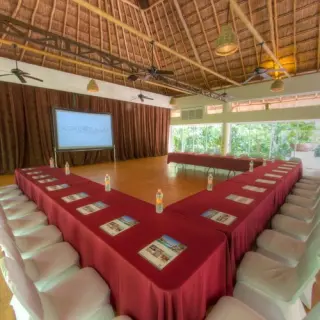 Indoor wedding reception venue with a palapa roof and U-shaped table setup at Kore Tulum, Tulum