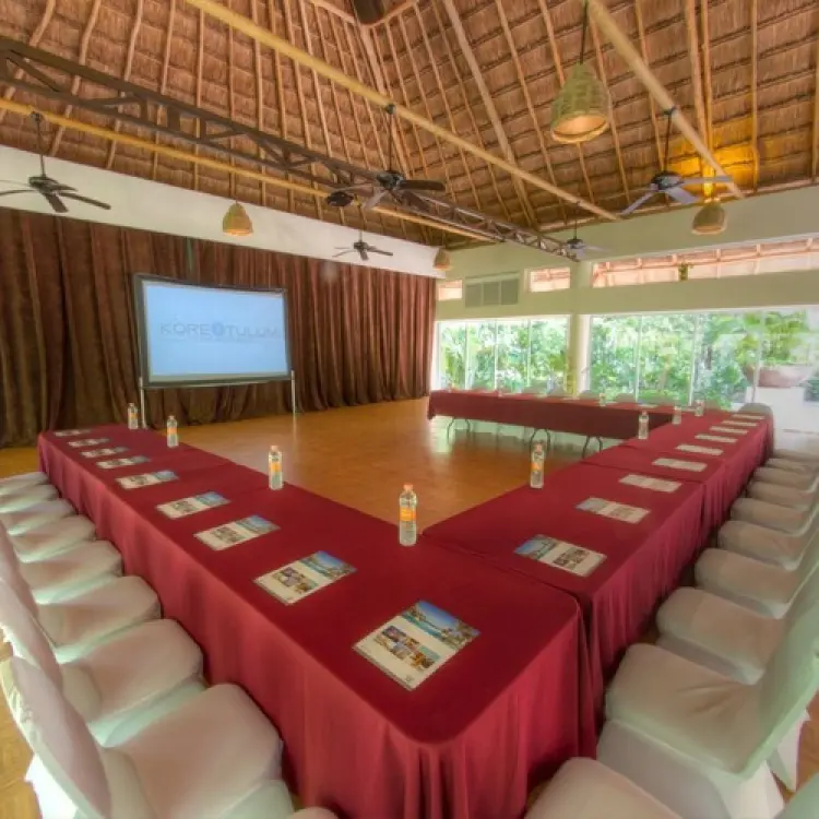 Indoor wedding reception venue with a palapa roof and U-shaped table setup at Kore Tulum, Tulum