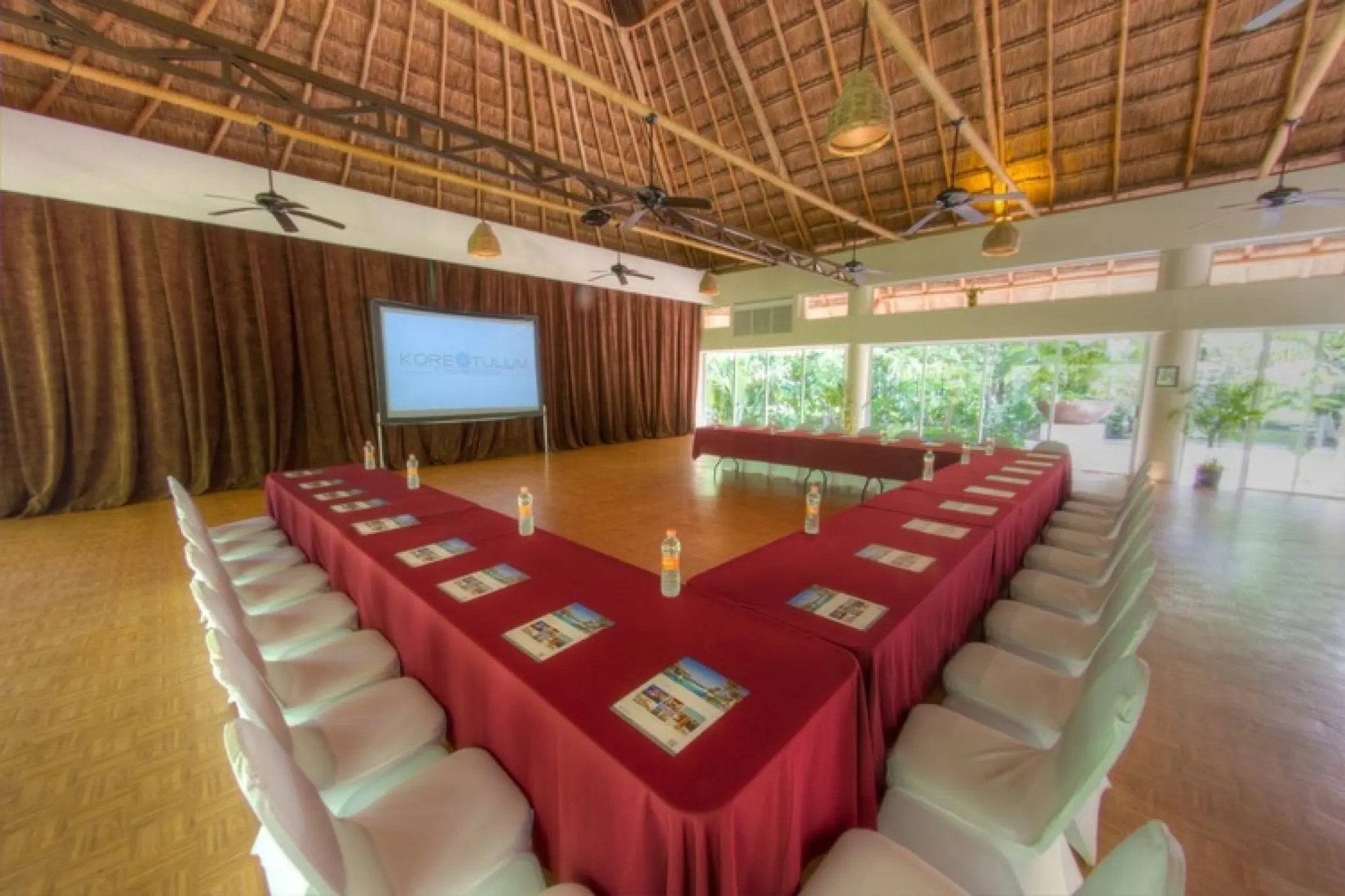 Indoor wedding reception venue with a palapa roof and U-shaped table setup at Kore Tulum, Tulum