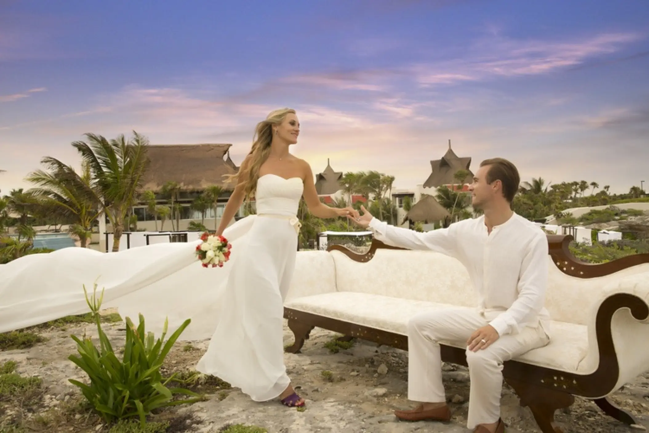 Bride and groom holding hands by a vintage sofa during sunset at Kore Tulum, Tulum