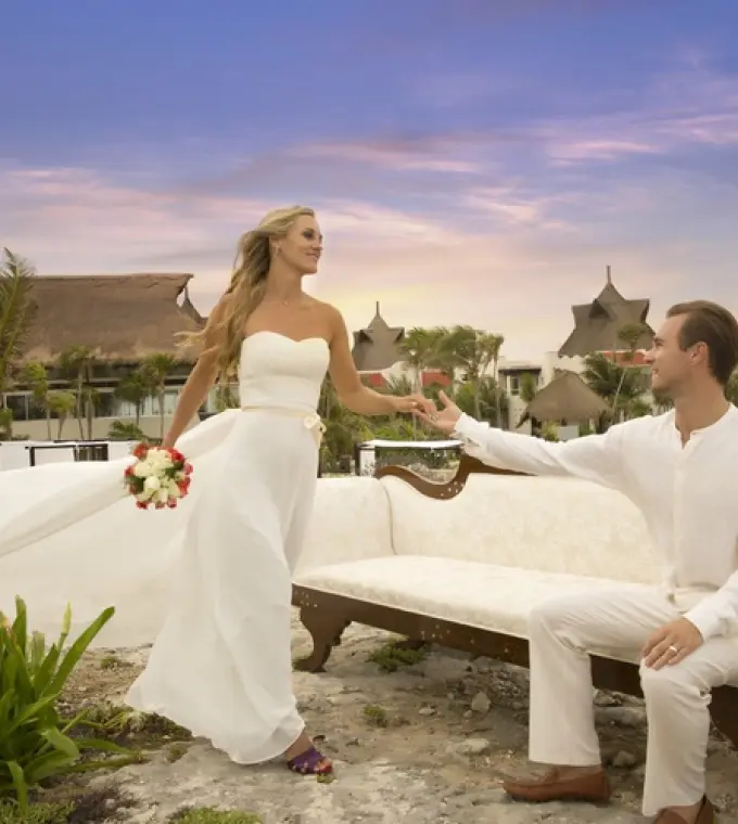 Bride and groom holding hands by a vintage sofa during sunset at Kore Tulum, Tulum