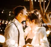 Groom kissing the bride's forehead during a wedding reception with string lights