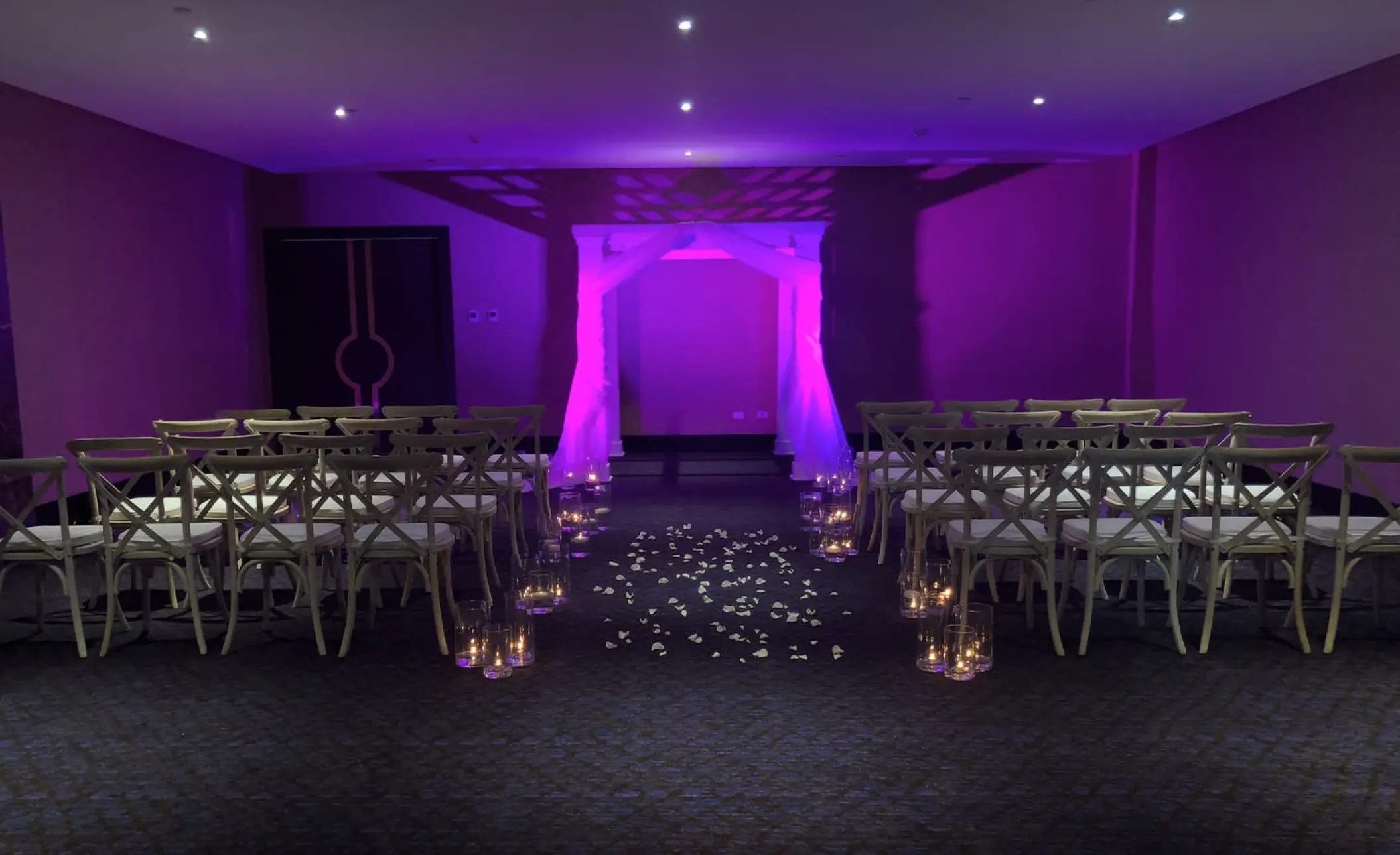 Indoor ballroom wedding ceremony with purple lighting and white fabric arch at Le Blanc Los Cabos, Cabo San Lucas