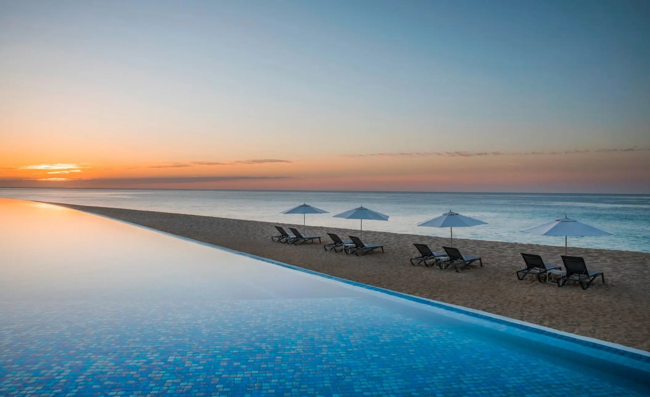 Infinity pool and beachfront lounge chairs at sunset at Le Blanc Los Cabos, Cabo San Lucas