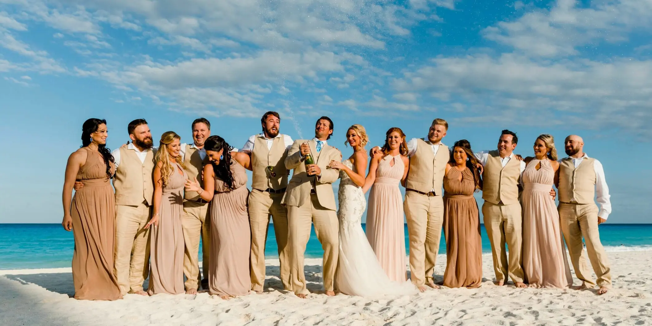 Wedding party cheering while the groom pops champagne on the beach at Le Blanc Los Cabos, Cabo San Lucas