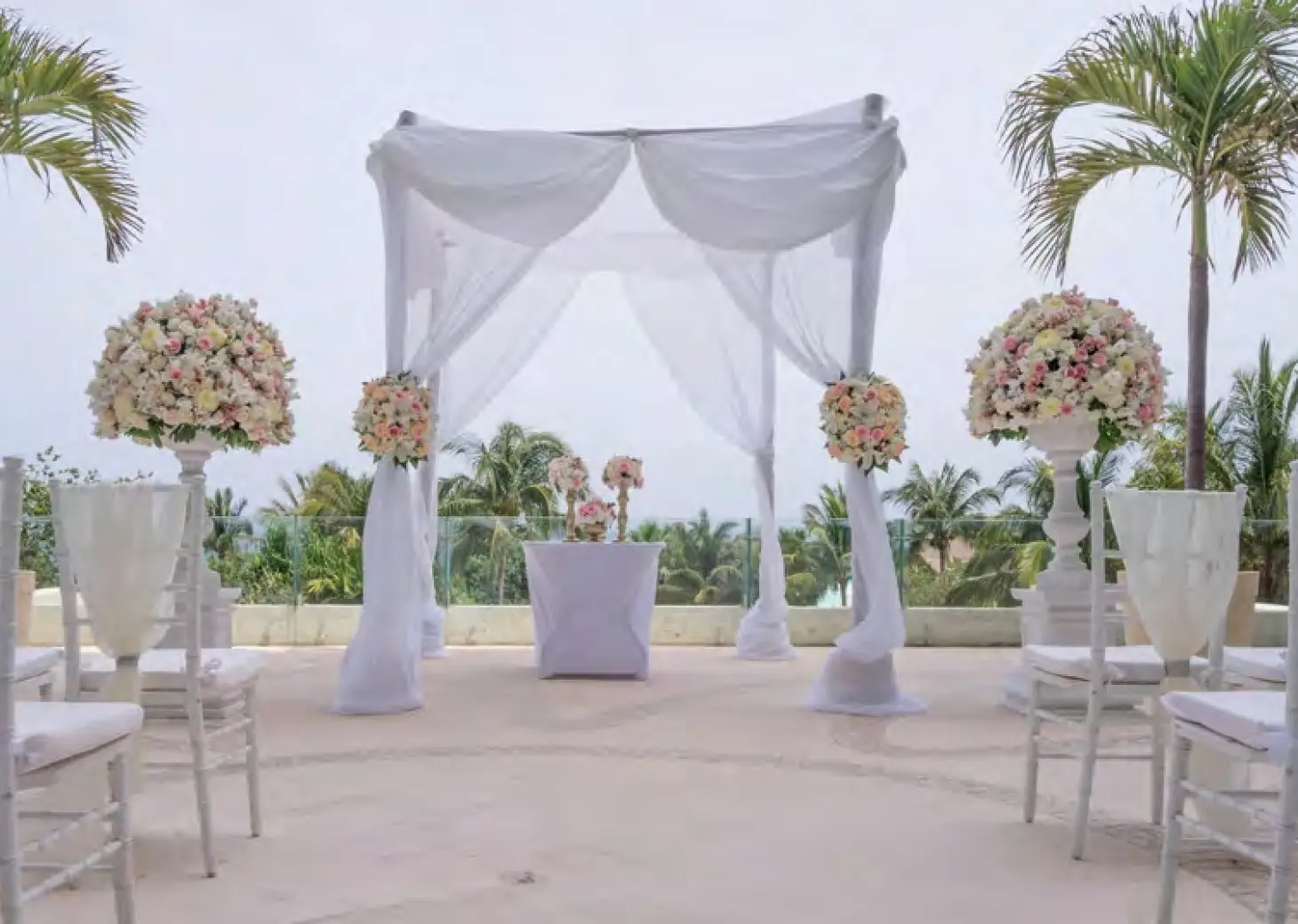 Outdoor terrace wedding ceremony setup with white draped chuppah and floral spheres at Live Aqua Cancun