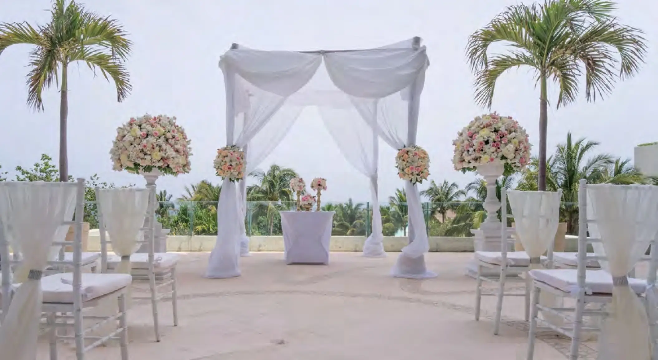 Outdoor terrace wedding ceremony setup with white draped chuppah and floral spheres at Live Aqua Cancun