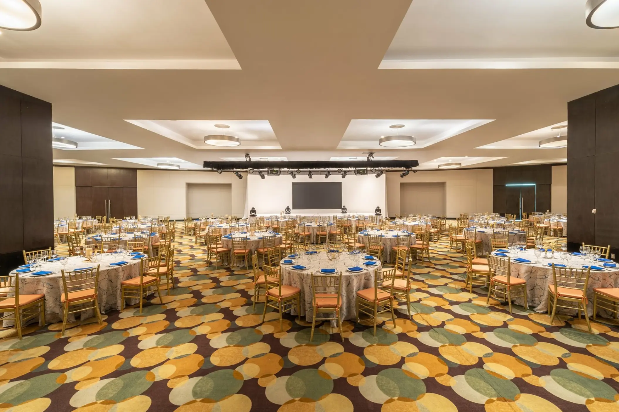 Indoor wedding reception ballroom with round tables and gold chairs at Live Aqua Cancun