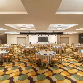Indoor wedding reception ballroom with round tables and gold chairs at Live Aqua Cancun