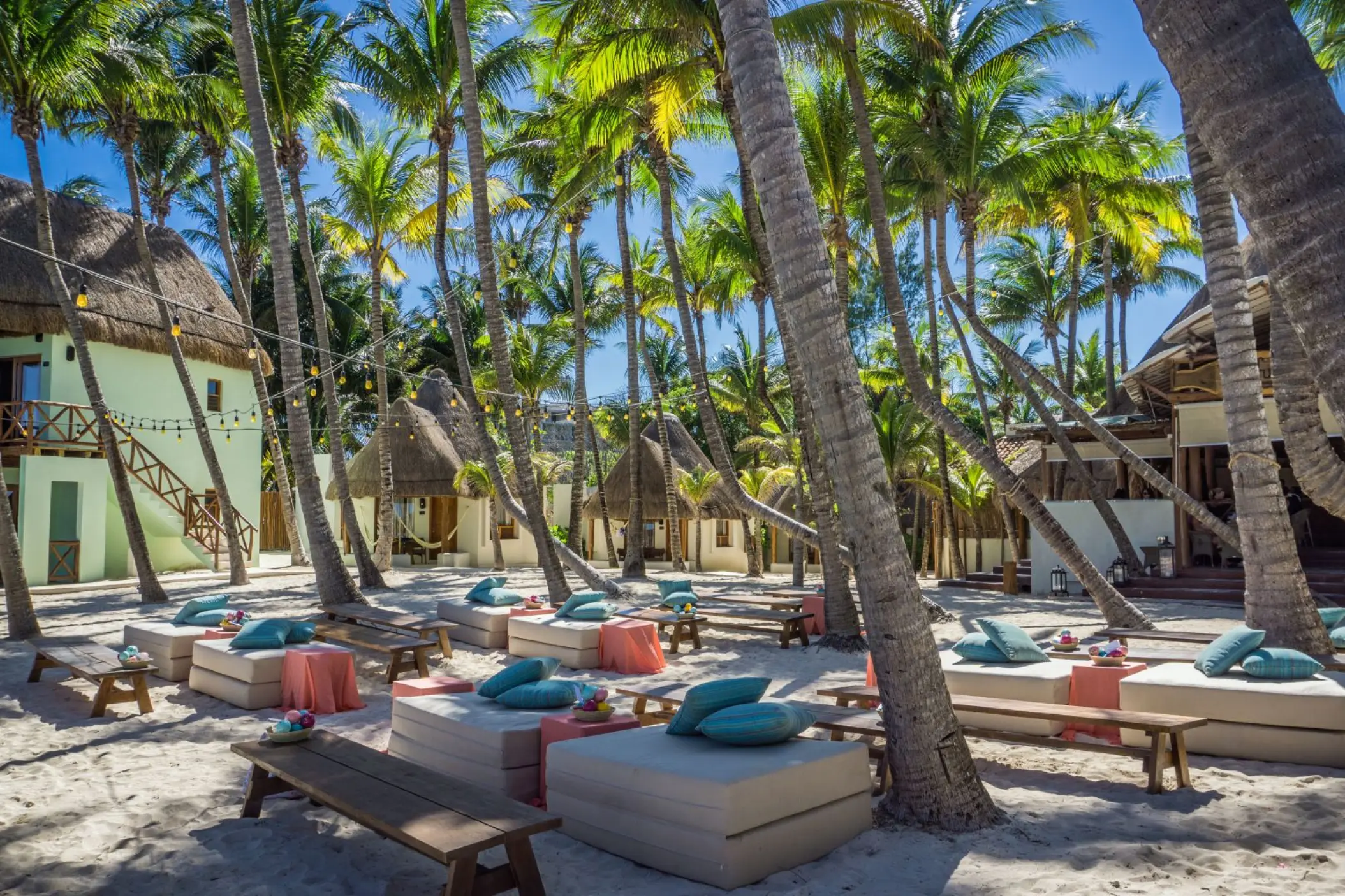 Beachfront lounge area with white daybeds and palm trees at Mahekal Beach Resort, Playa Del Carmen