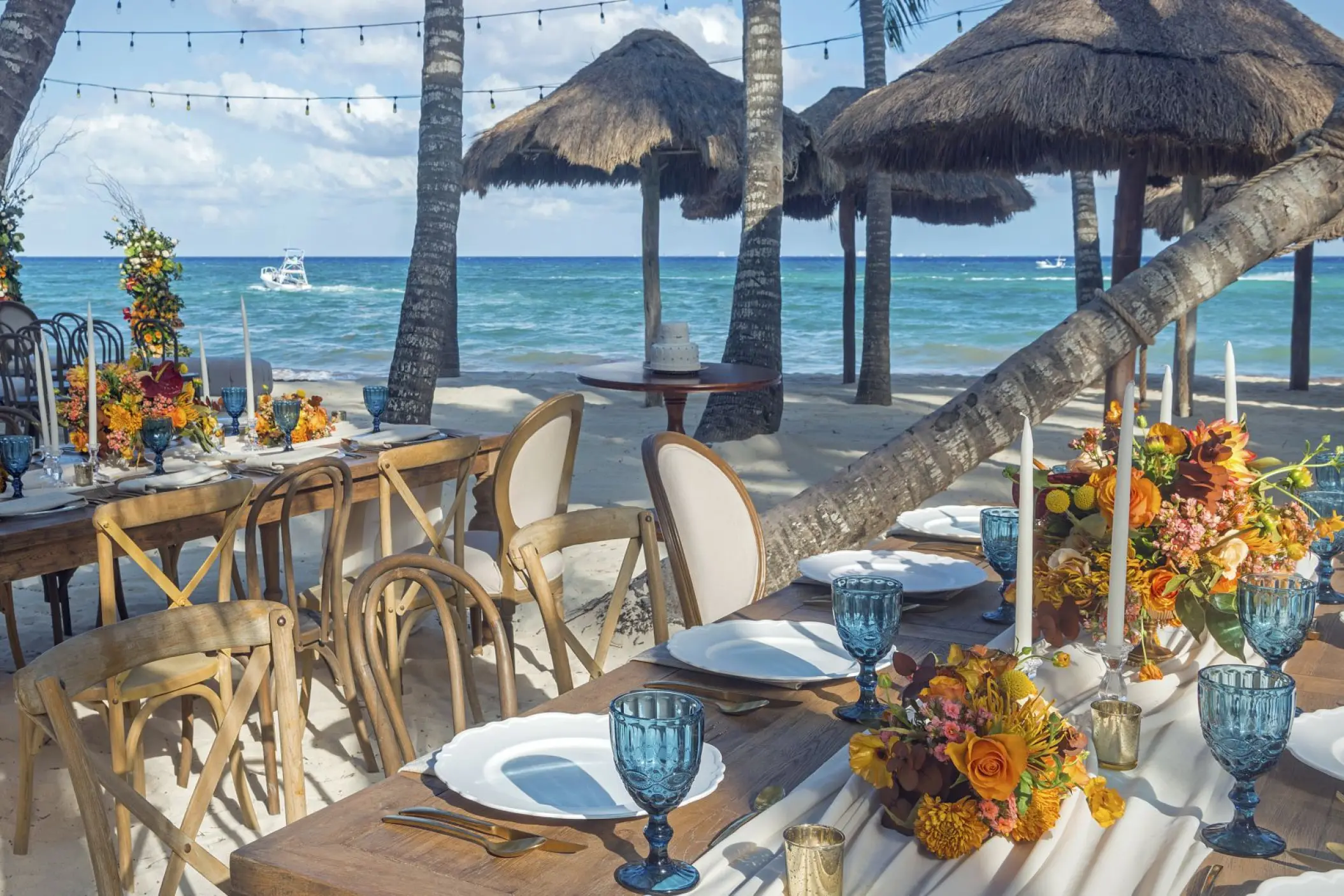 Beachfront wedding reception tables with blue glassware and floral centerpieces at Mahekal Beach Resort, Playa Del Carmen