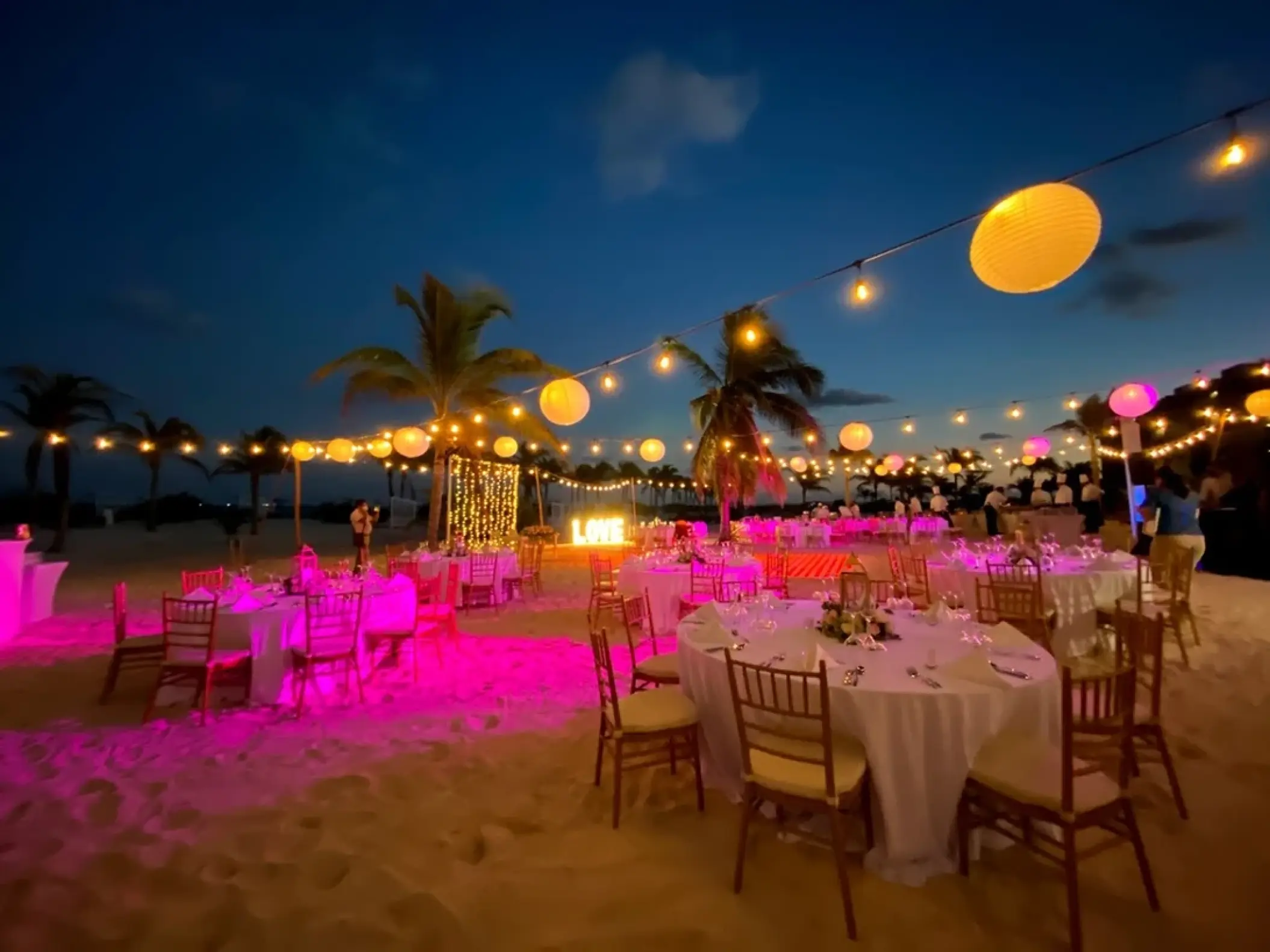 Beachfront wedding reception at night with pink lighting and paper lanterns at Majestic Elegance Costa Mujeres, Cancun