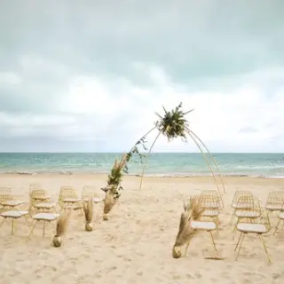 Beachfront wedding ceremony with a pampas grass arch and gold chairs at Majestic Mirage Costa Mujeres, Cancun