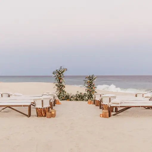 Beachfront wedding ceremony with wooden benches and floral arch at Mar Del Cabo, Cabo San Lucas