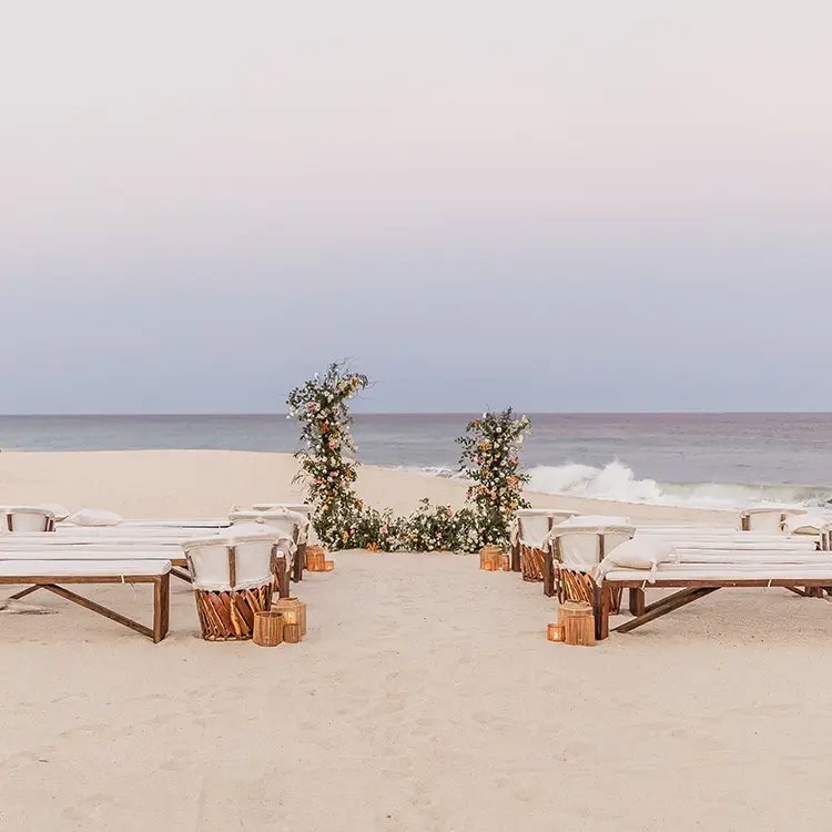 Beachfront wedding ceremony with wooden benches and floral arch at Mar Del Cabo, Cabo San Lucas