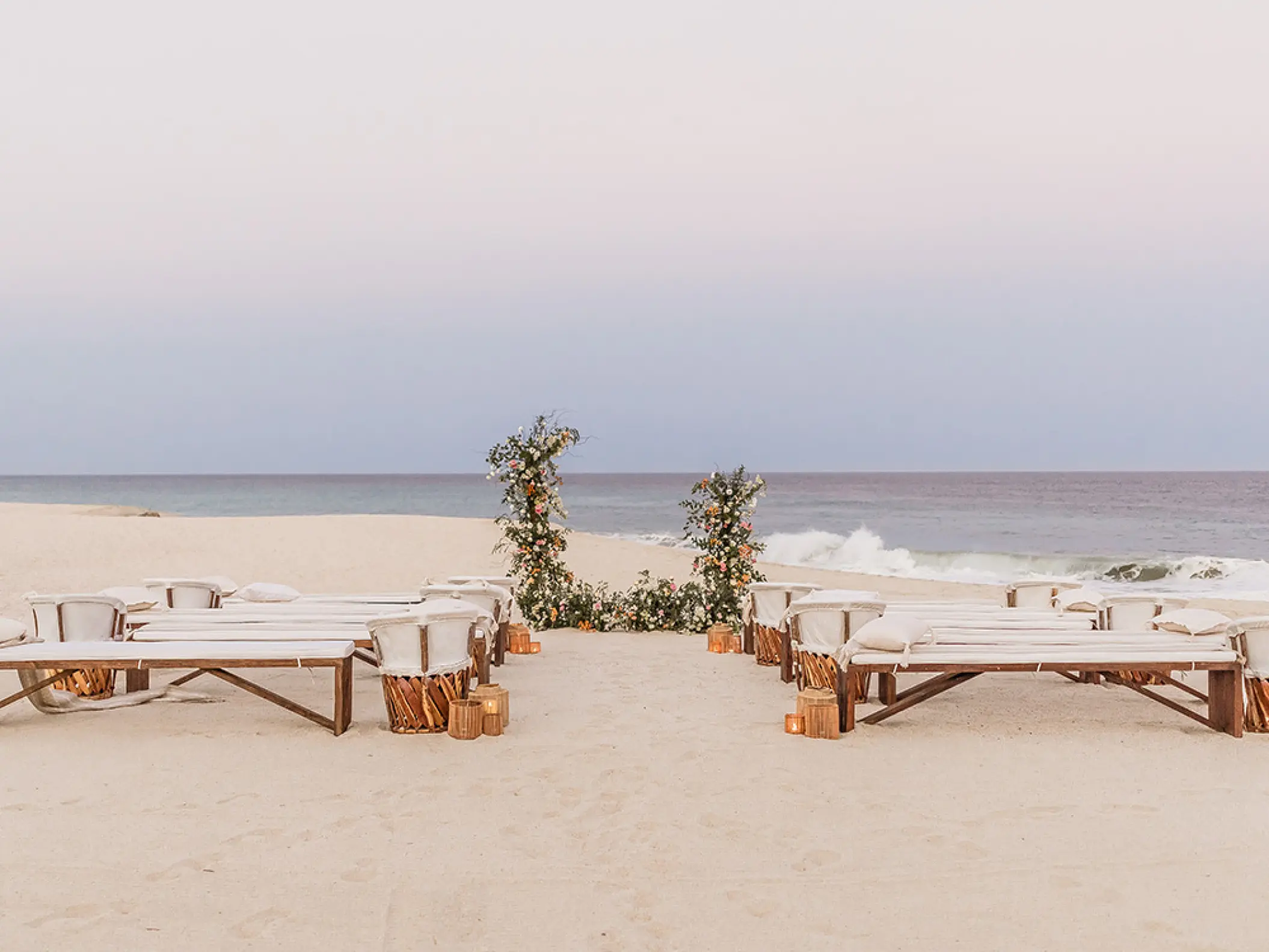 Beachfront wedding ceremony with wooden benches and floral arch at Mar Del Cabo, Cabo San Lucas