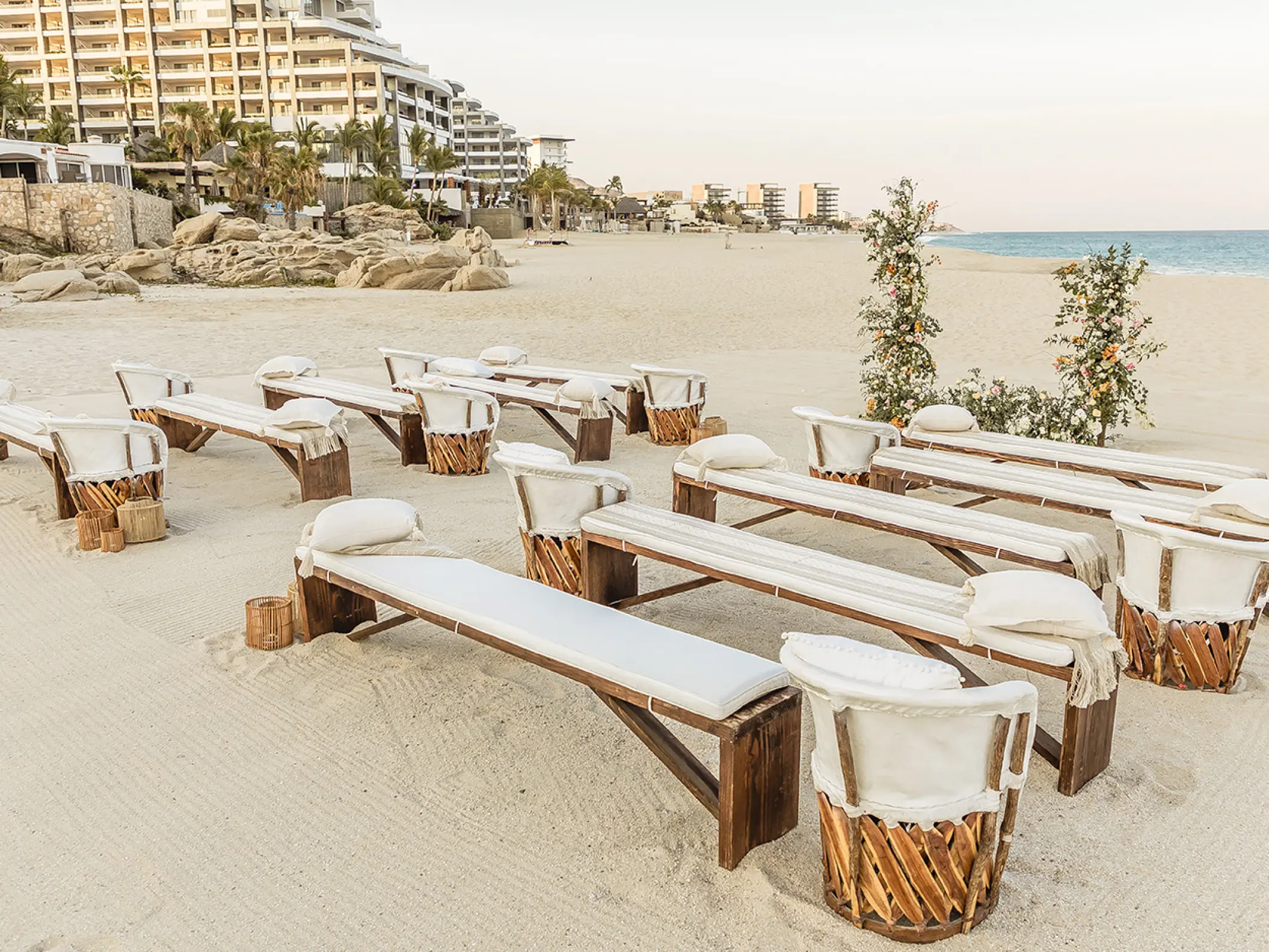 Beachfront wedding ceremony with wooden benches and white cushions at Mar Del Cabo, Cabo San Lucas