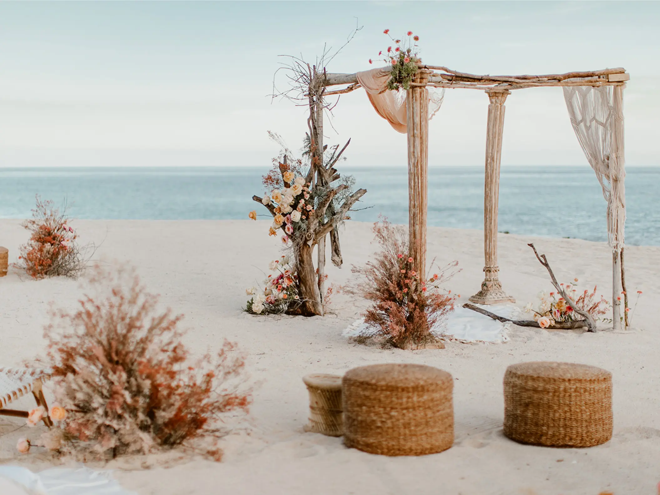 Beach wedding ceremony setup with wooden arch and boho decor at Mar Del Cabo, Cabo San Lucas