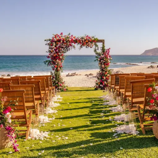 Oceanfront wedding ceremony with a floral arch and wooden chairs at Mar Del Cabo, Cabo San Lucas