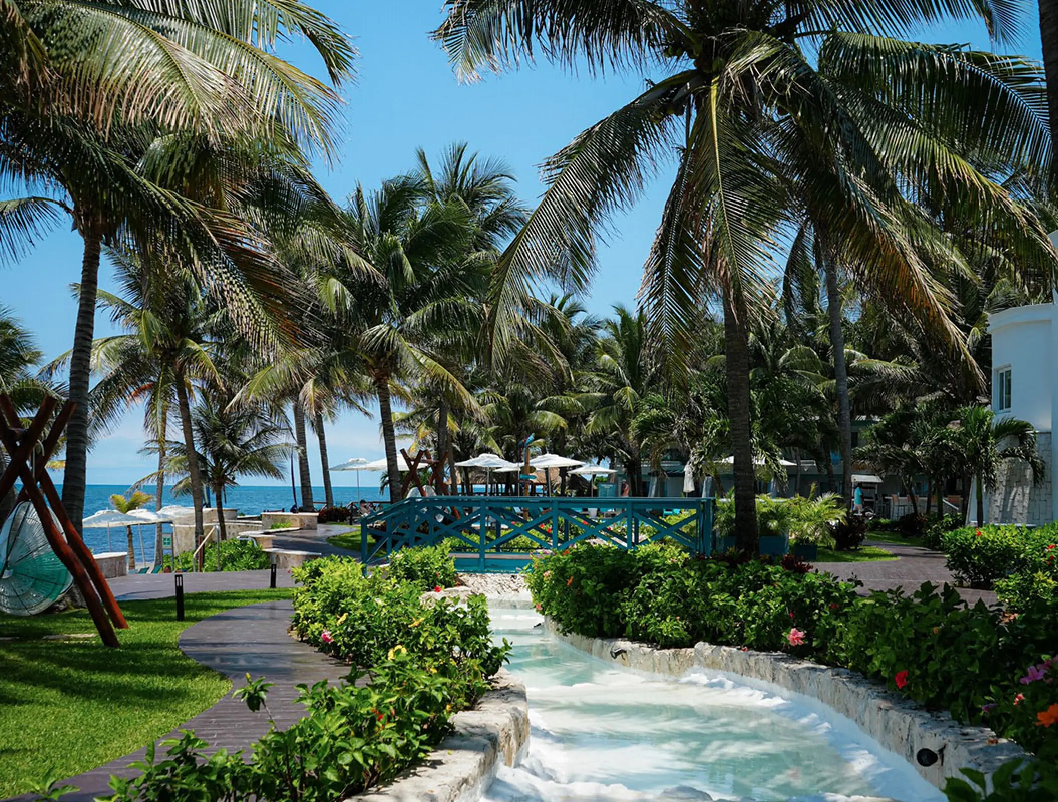 Palm tree lined gardens and blue wooden bridge at Margaritaville Island Reserve Riviera Cancun