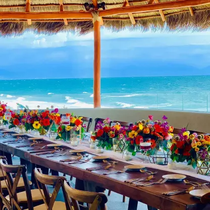Long wooden reception table under a palapa with colorful floral centerpieces at Armony Marival, Puerto Vallarta