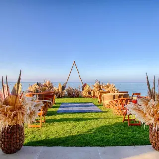 Beachfront wedding ceremony on a lawn with pampas grass and triangular arch at Armony Marival, Puerto Vallarta