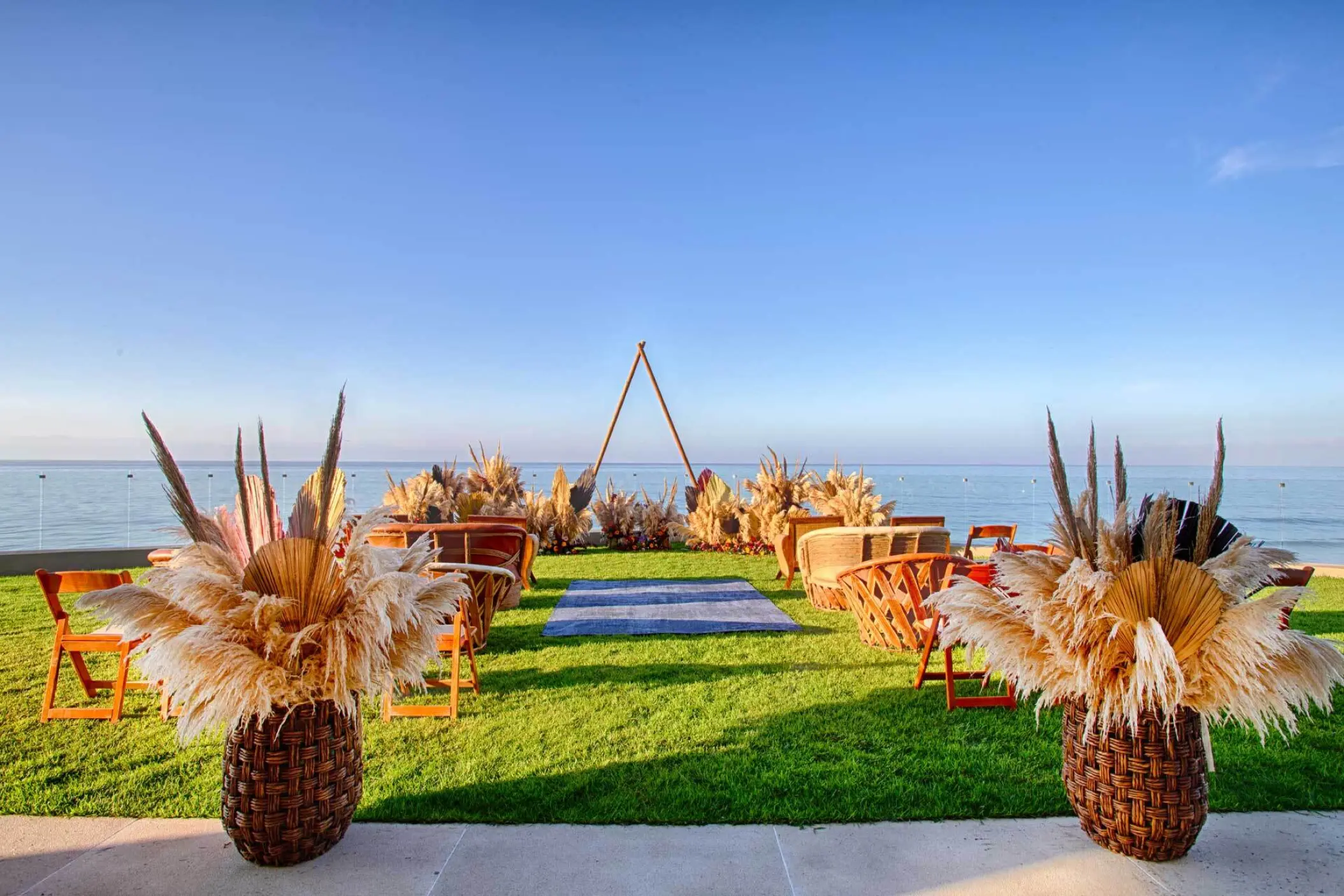 Beachfront wedding ceremony on a lawn with pampas grass and triangular arch at Armony Marival, Puerto Vallarta