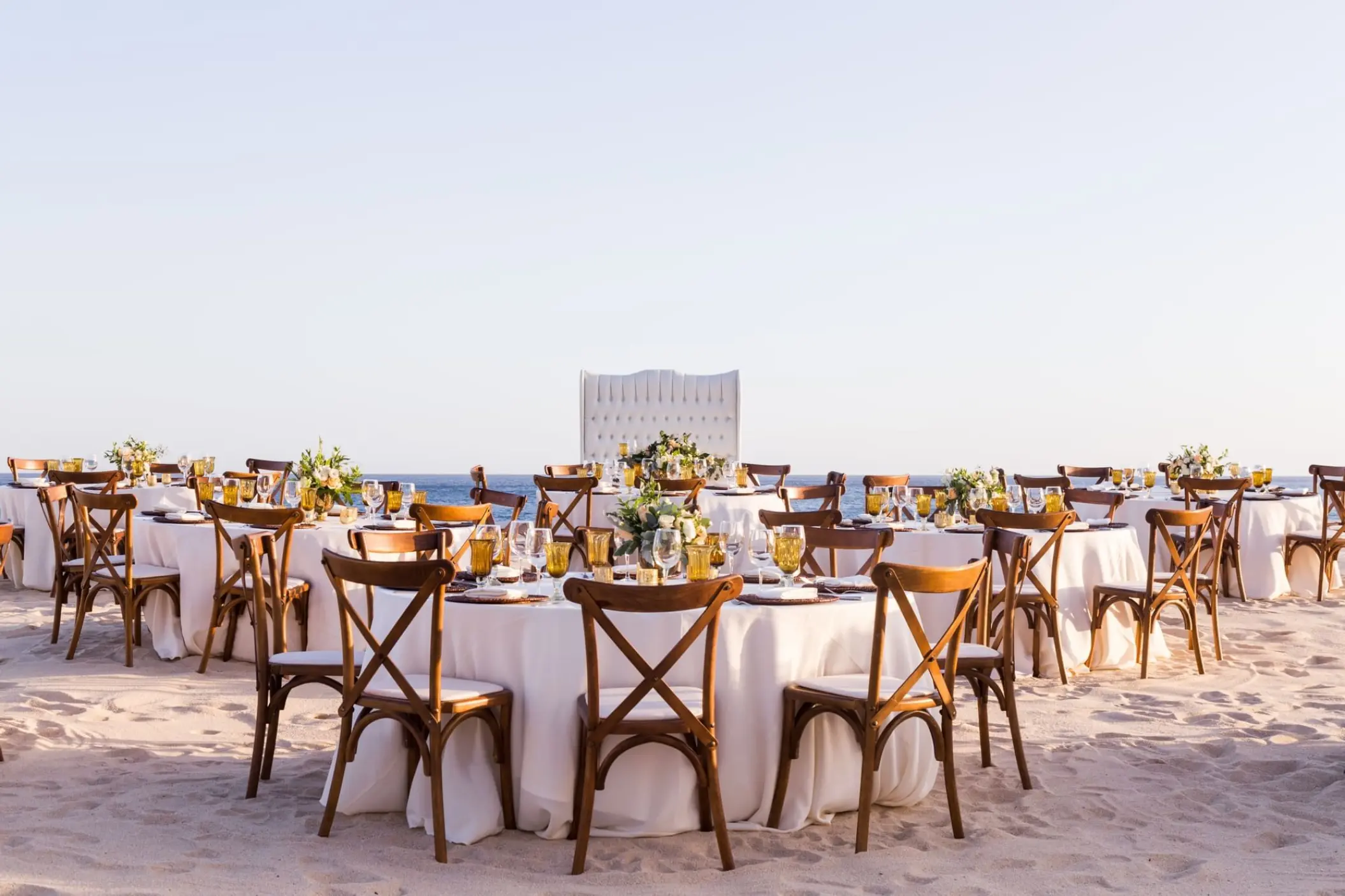 Beachfront wedding reception with wooden cross-back chairs and white linens at Marquis Los Cabos, Cabo San Lucas