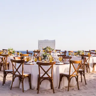 Beachfront wedding reception with wooden cross-back chairs and white linens at Marquis Los Cabos, Cabo San Lucas