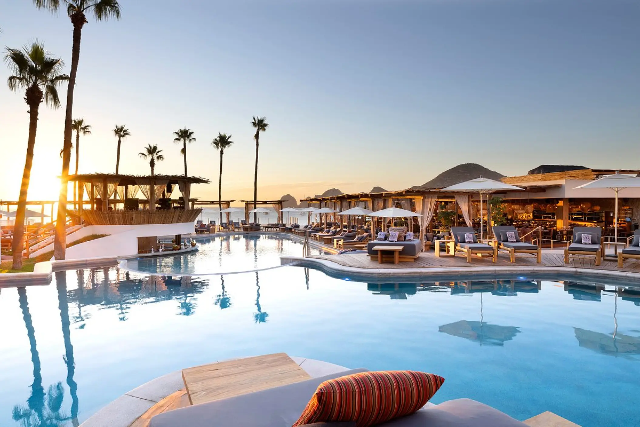 Pool area at ME Cabo with lounge chairs and palm trees at sunset, Cabo San Lucas