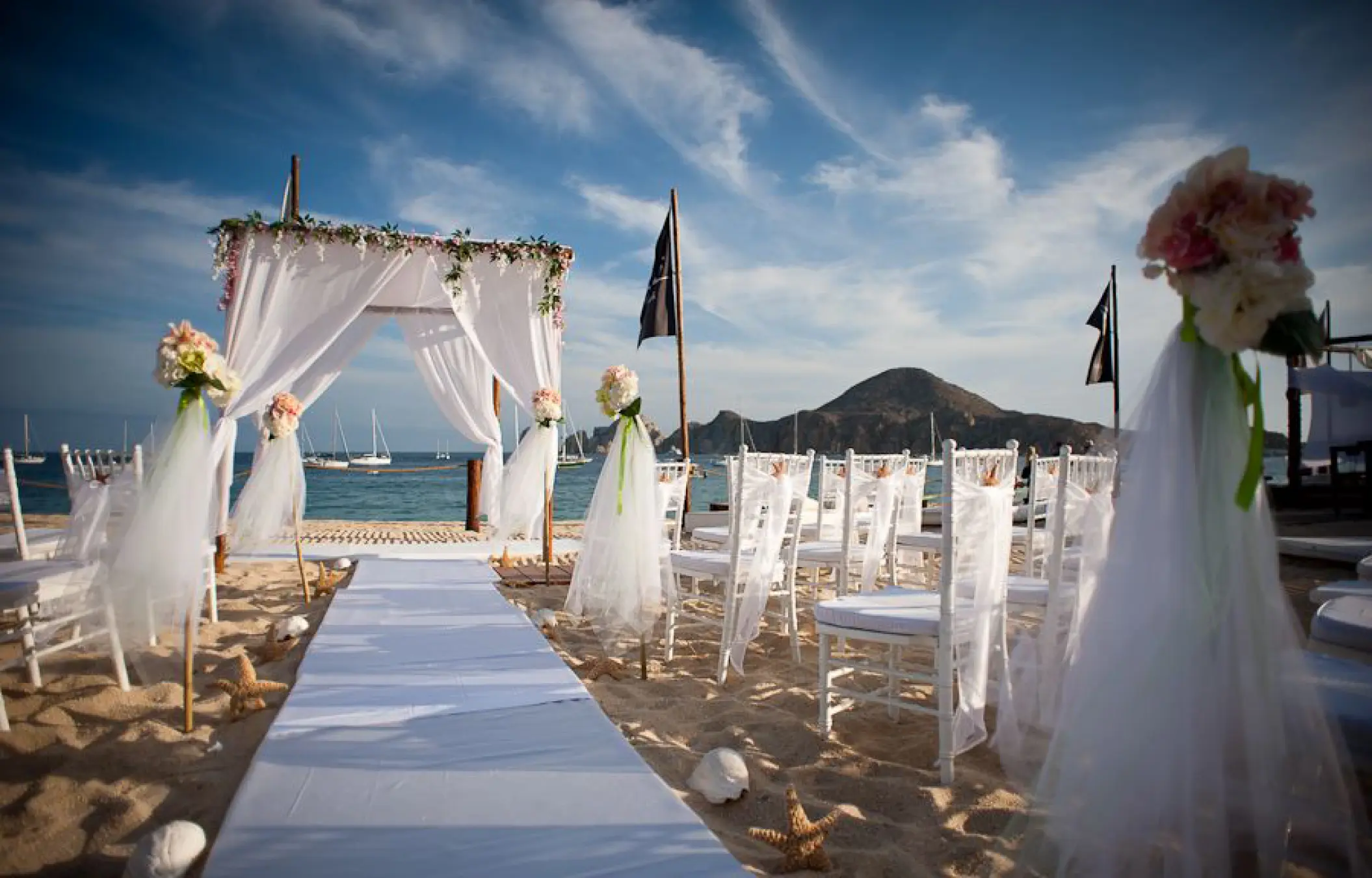 Beachfront wedding ceremony with white huppah and chairs at ME Cabo, Cabo San Lucas