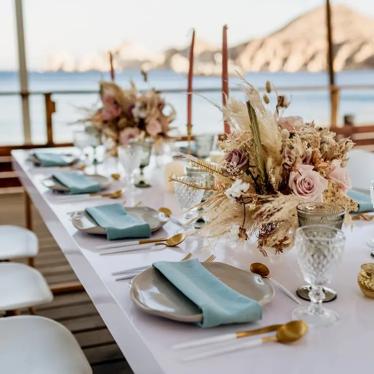Terrace wedding reception at ME Cabo with floral centerpieces and ocean views, Cabo San Lucas