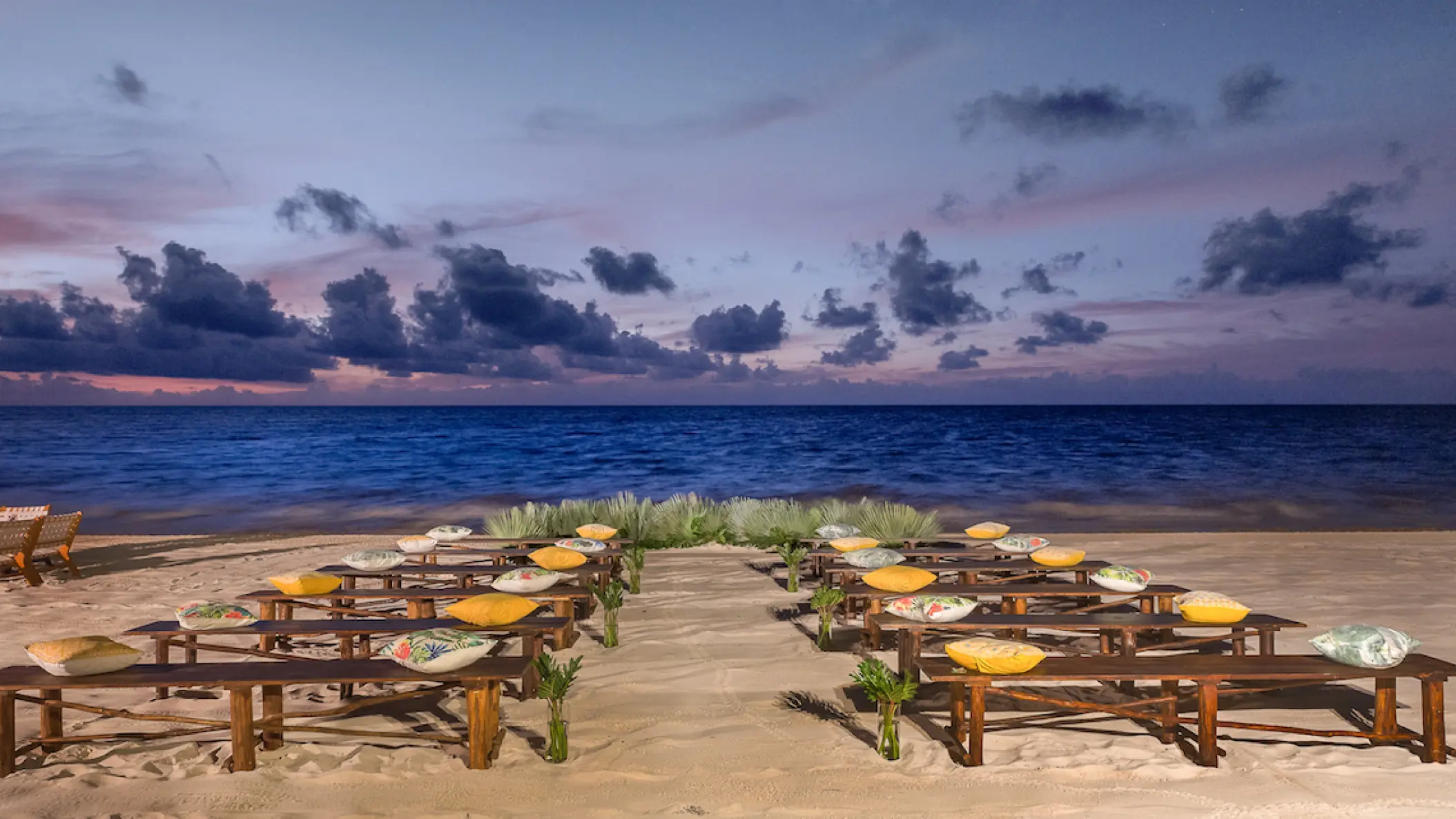 Beachfront wedding ceremony with wooden benches and yellow cushions at Moon Palace Cancun
