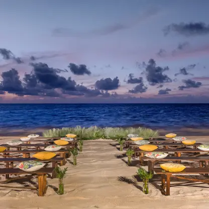 Beachfront wedding ceremony with wooden benches and yellow cushions at Moon Palace Cancun