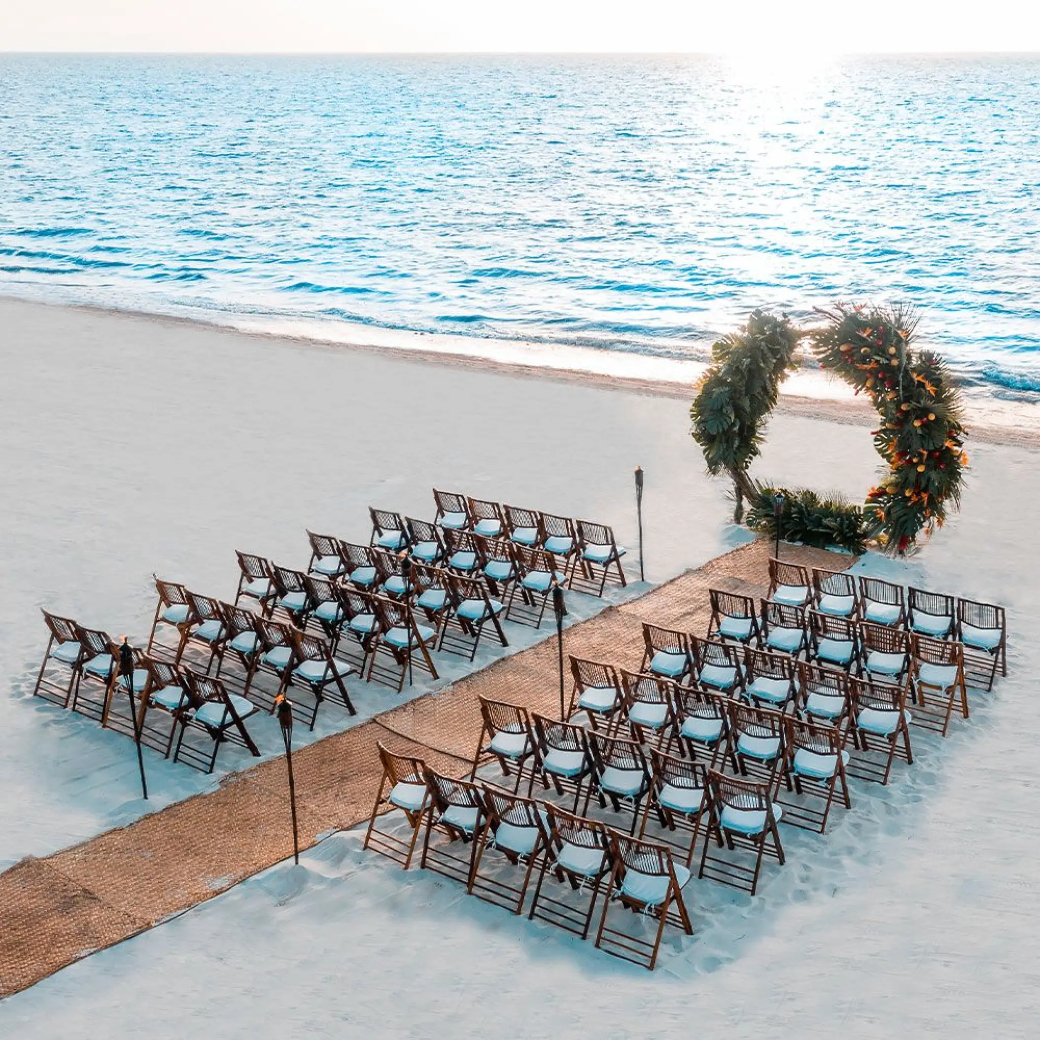 Beachfront wedding ceremony setup with a circular floral arch and wooden chairs at Moon Palace Cancun