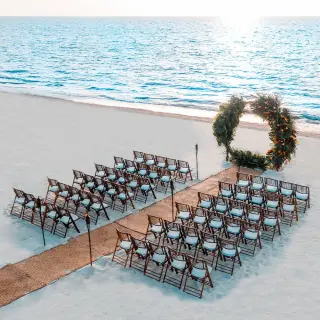 Beachfront wedding ceremony setup with a circular floral arch and wooden chairs at Moon Palace Cancun