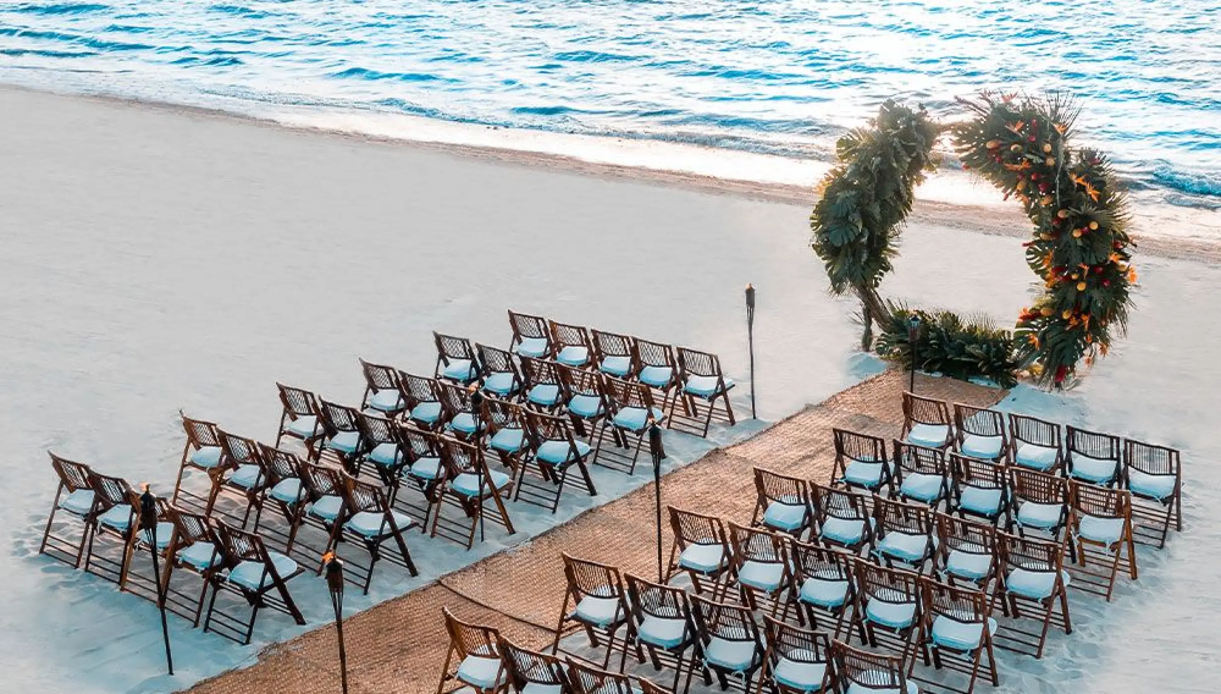 Beachfront wedding ceremony with circular floral arch and wooden chairs at Moon Palace Cancun