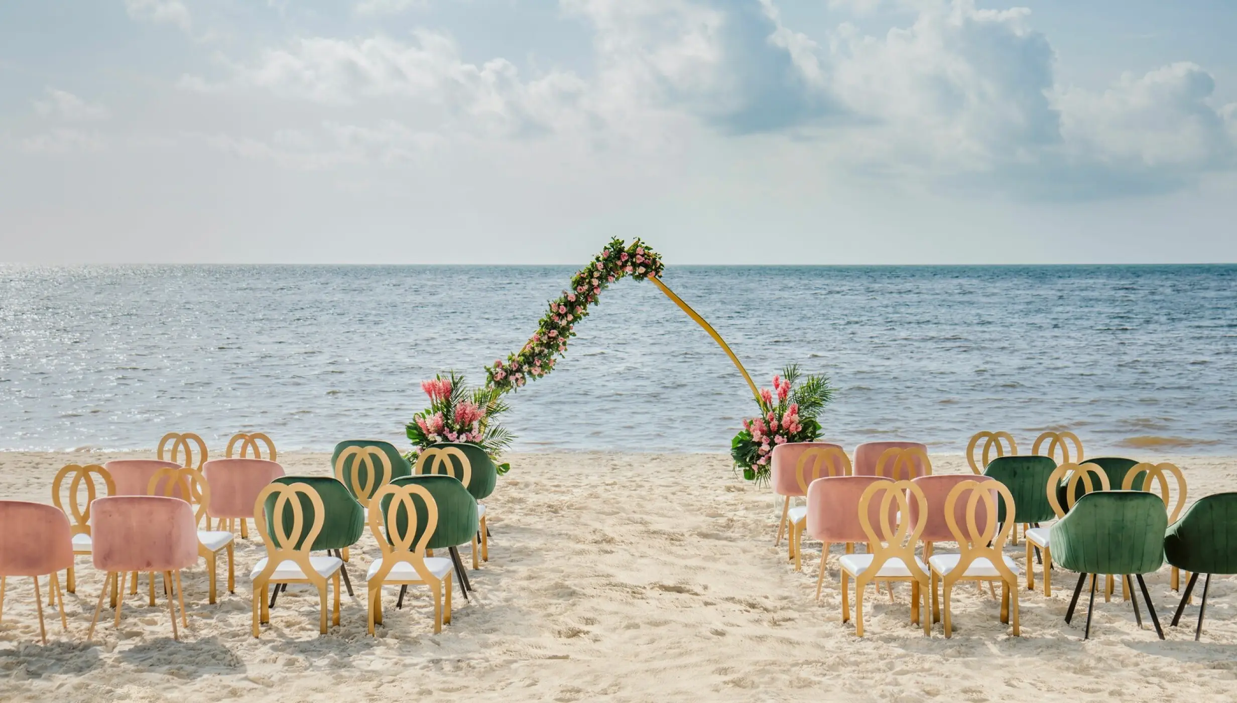Beachfront wedding ceremony with velvet chairs and a floral arch at Moon Palace Cancun