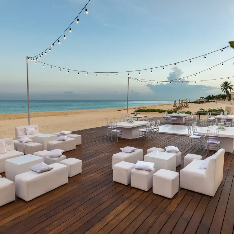 Outdoor wedding reception lounge with white furniture on a wooden deck at Moon Palace Cancun