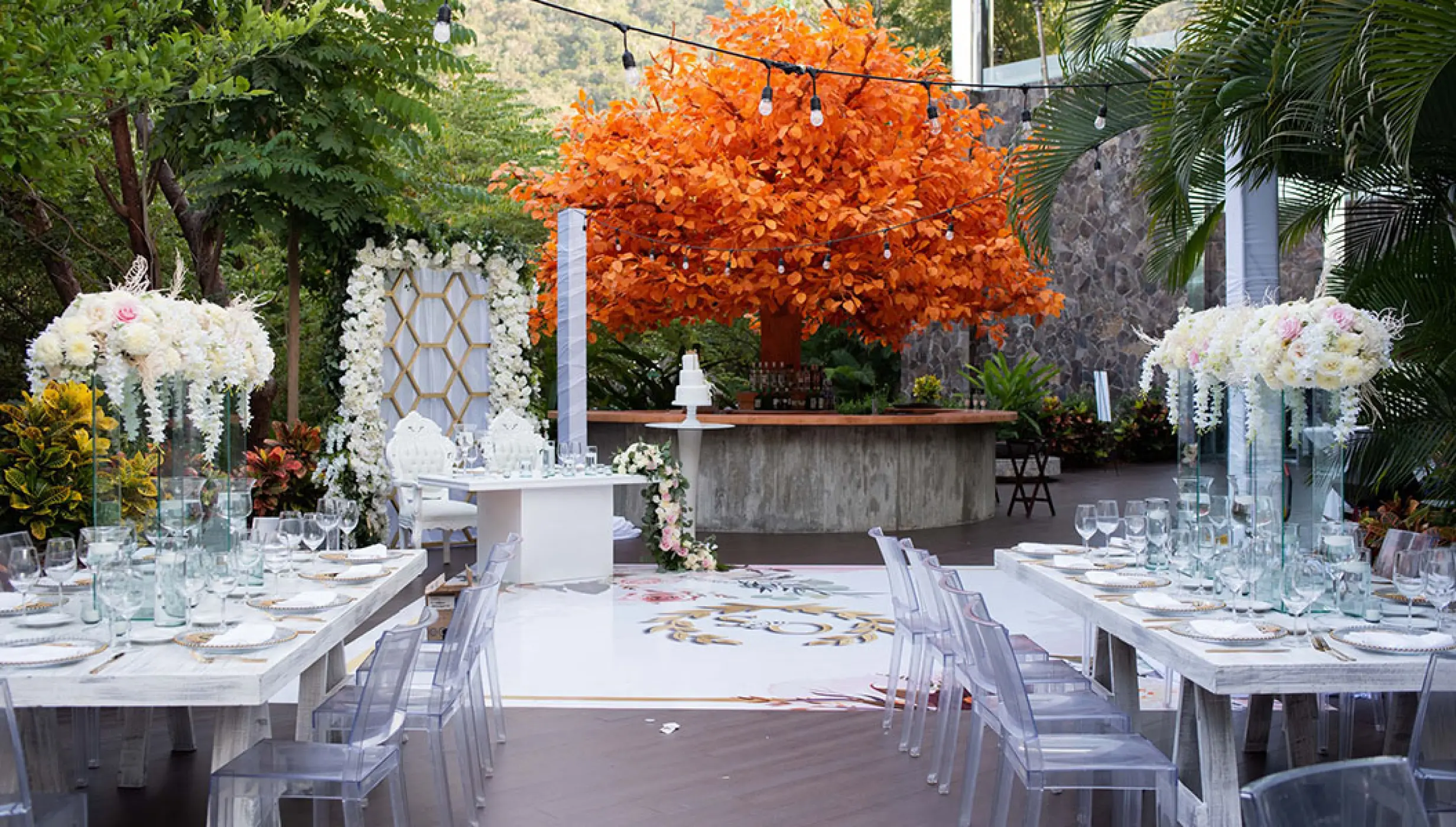 Outdoor wedding reception setup with white tables and a bright orange tree at Garza Blanca, Puerto Vallarta