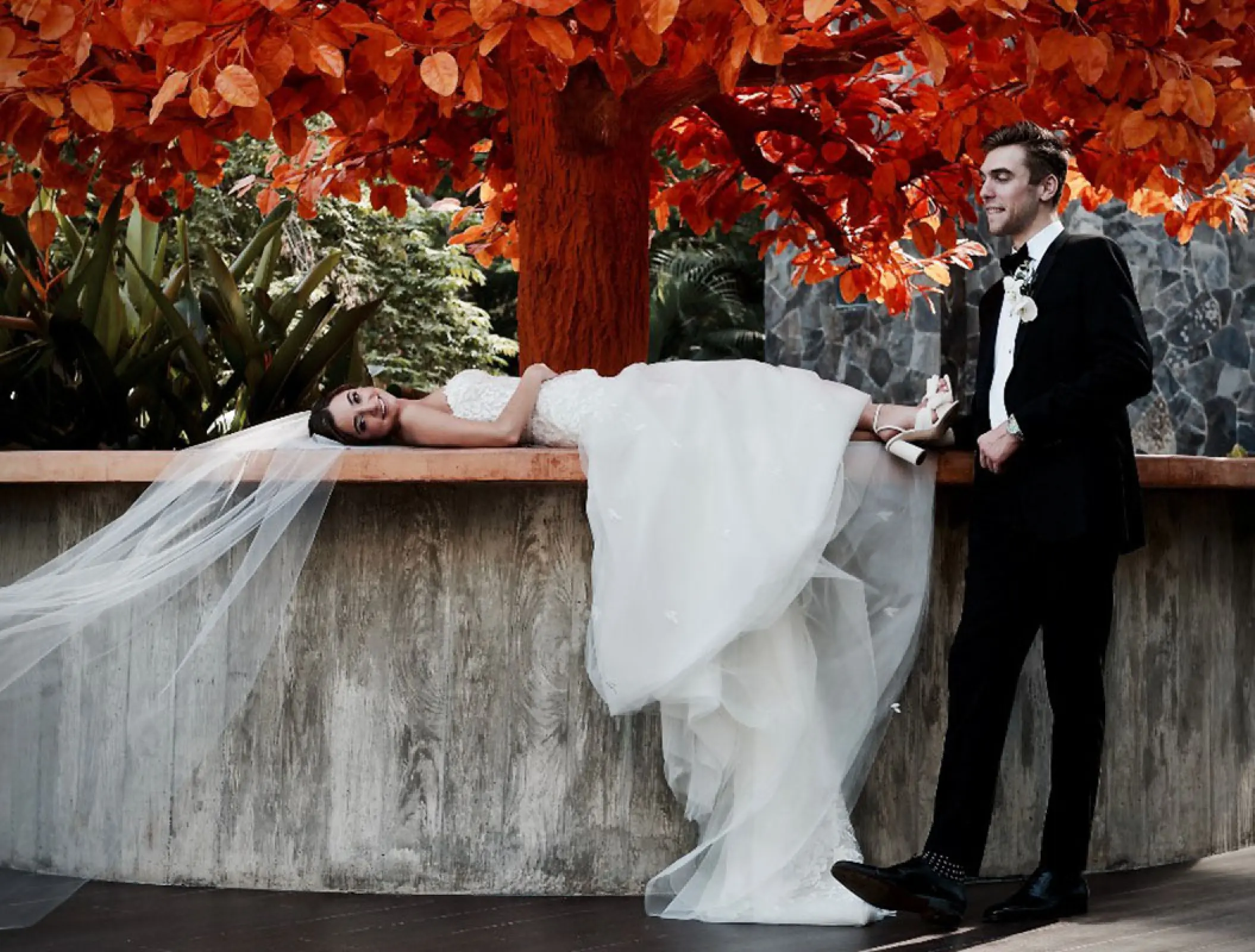 Bride lying on a stone ledge under an orange tree with the groom at Garza Blanca Preserve, Puerto Vallarta