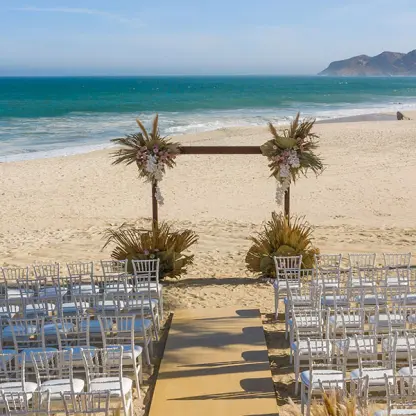 Beachfront wedding ceremony with white chairs and a wooden arch at Hotel Mousai, Puerto Vallarta