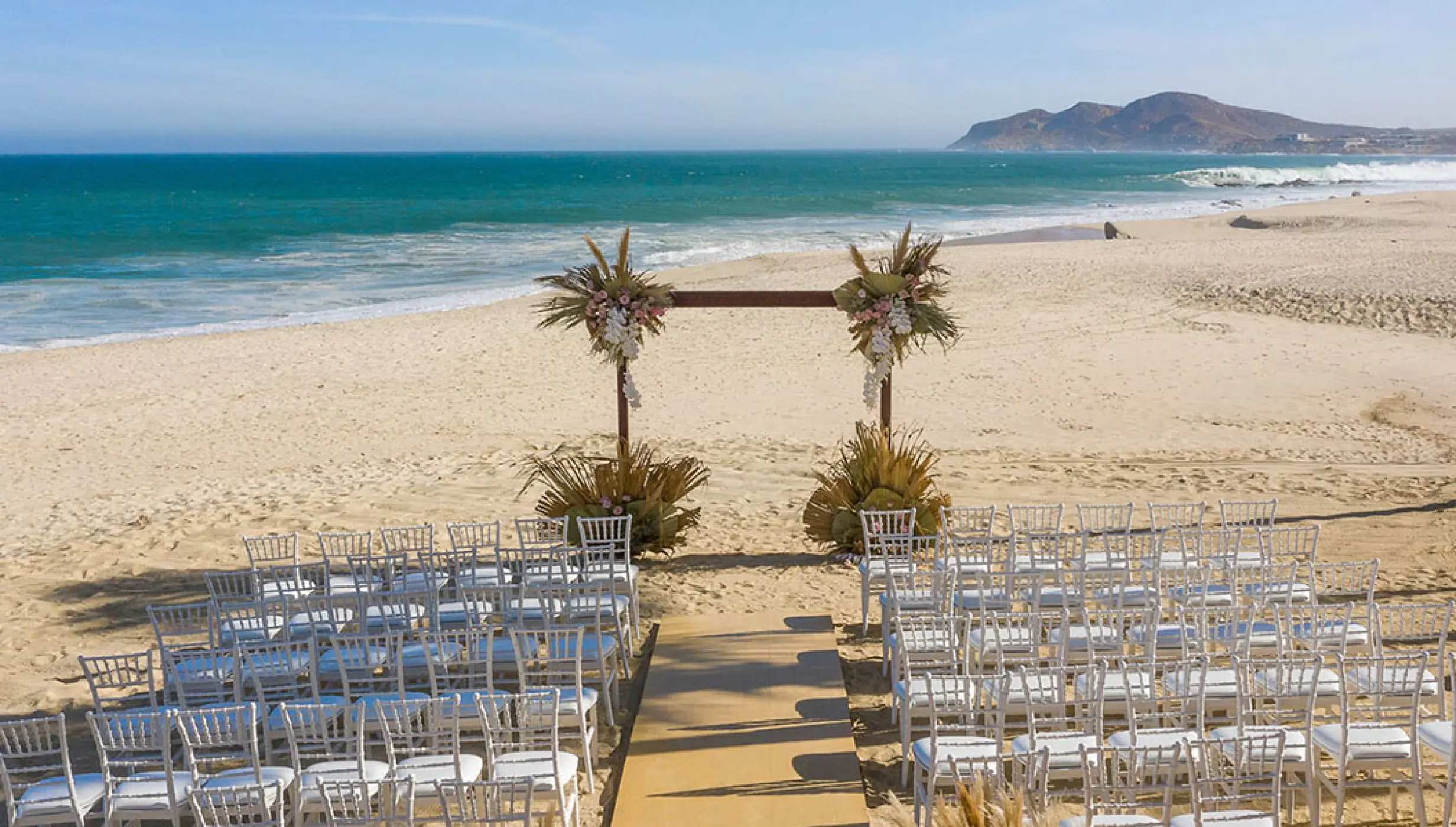 Beachfront wedding ceremony with a wooden arch and white chairs at Hotel Mousai, Puerto Vallarta