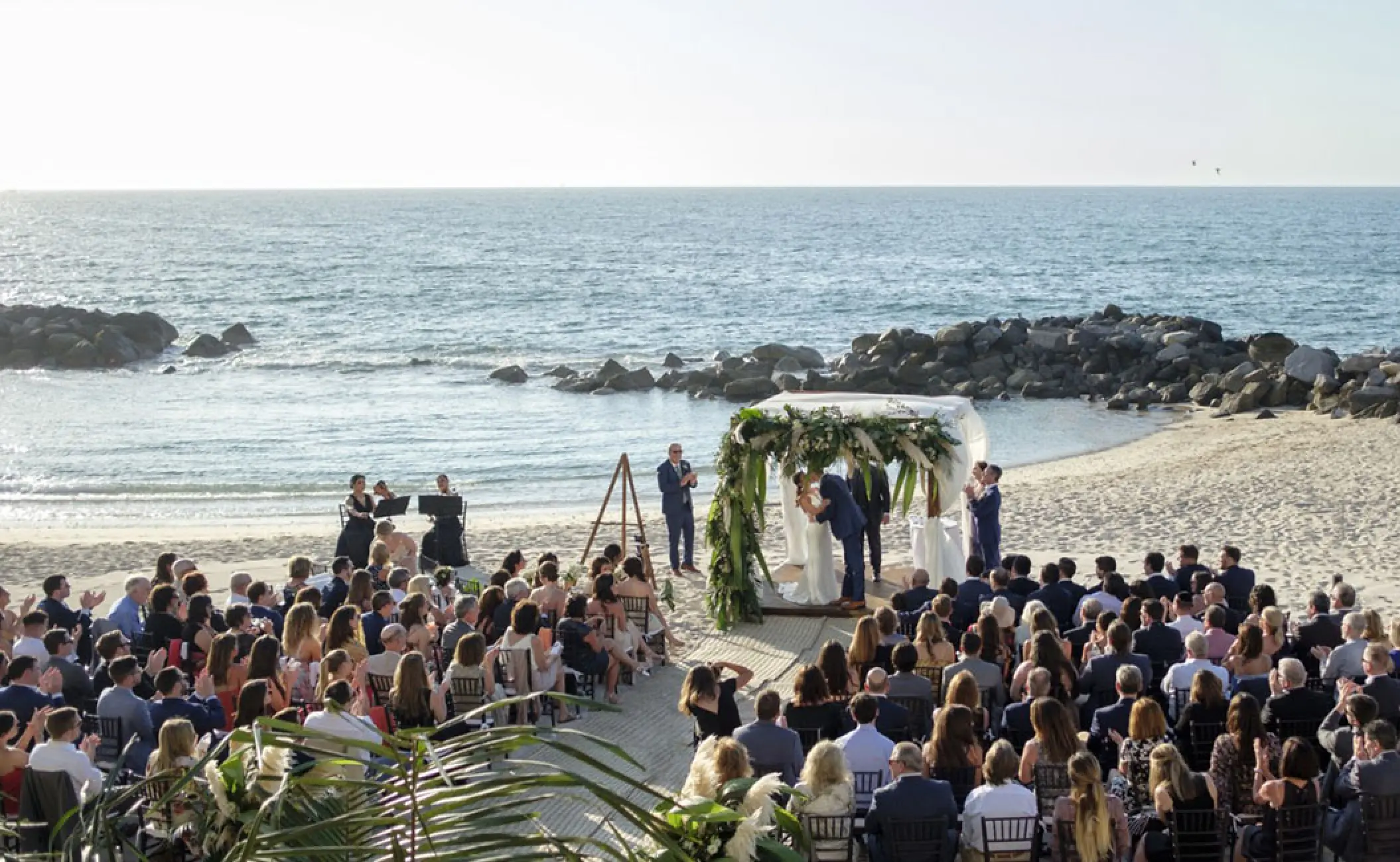 Beachfront wedding ceremony with guests under a tropical huppah at Hotel Mousai, Puerto Vallarta