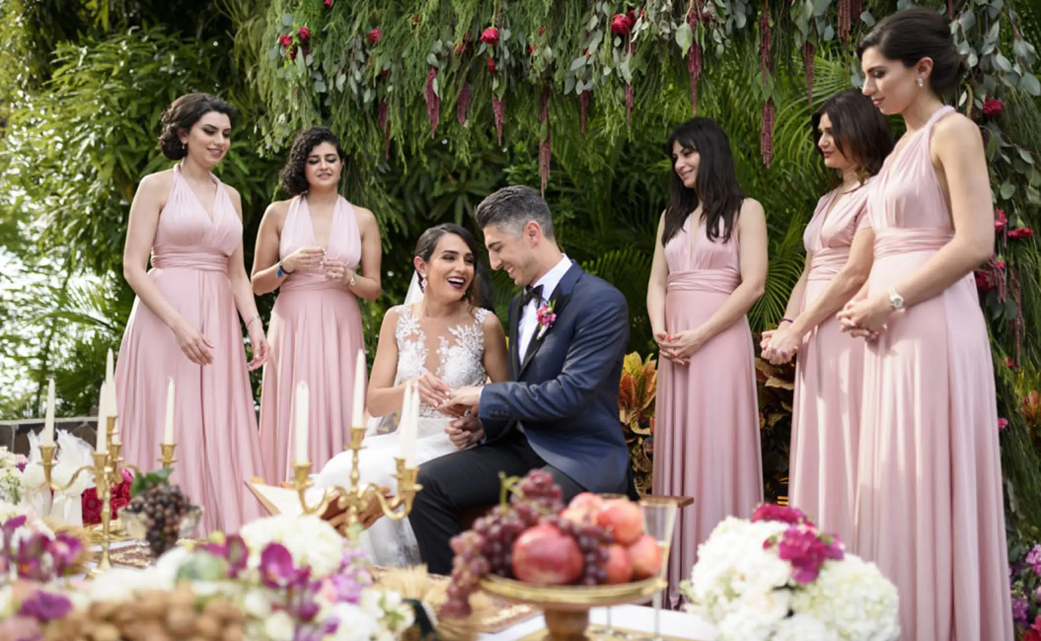 The bride and groom exchange rings surrounded by bridesmaids in pink at Hotel Mousai, Puerto Vallarta