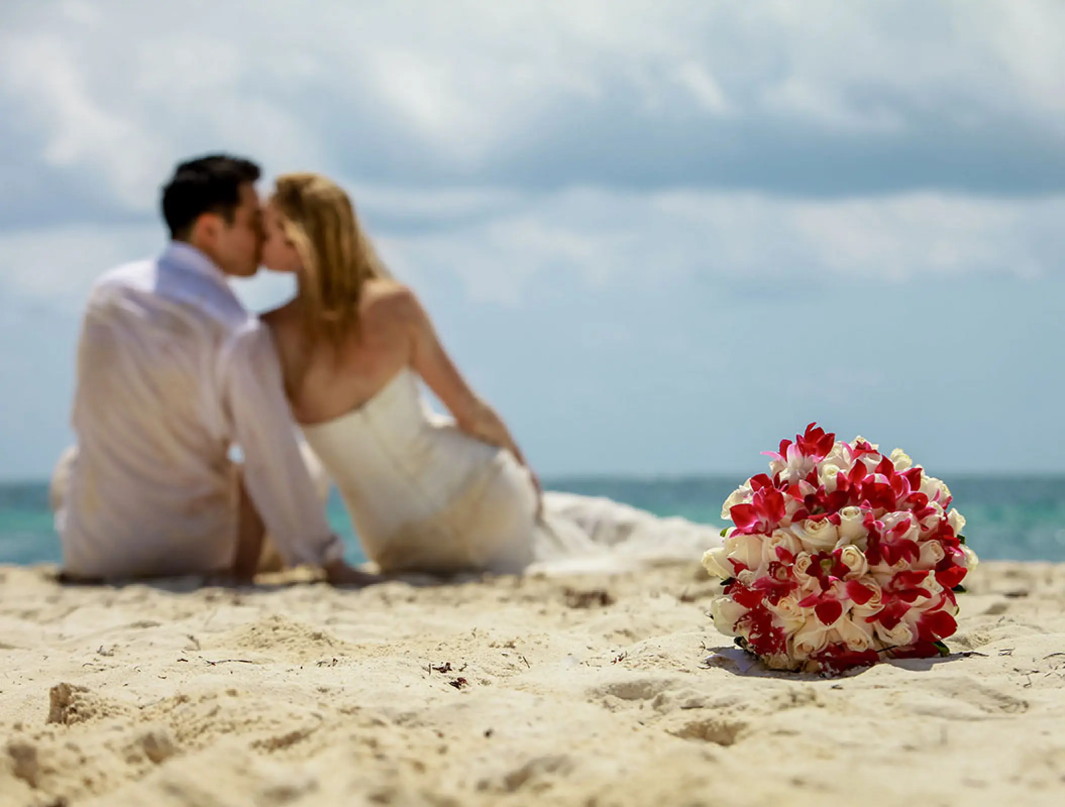 Red and white orchid bouquet on the sand with a couple kissing at Conrad Tulum, Tulum